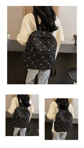 Detail of quilted black nylon backpack featuring white embroidered bow patterns and zippers