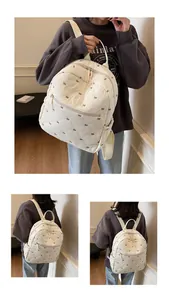 Detail of white quilted backpack featuring brown bow embroidery and a front zipper pocket