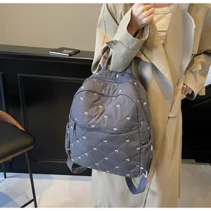 Close-up of dark grey quilted backpack featuring white bow print and diamond stitching