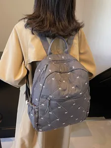 Grey quilted nylon backpack with white bow embroidery and adjustable straps for women