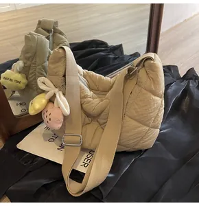 Detail van beige gewatteerde schoudertas met pluche hangers en geweven draagriem