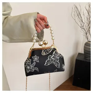Detalle de bordado de mariposas blancas y flores en bolso de satén negro con asa de perlas