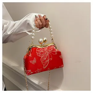 Detalle del bolso de seda roja con bordado de mariposa y elegante asa de perlas