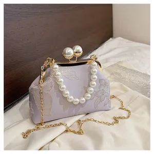 Detalle de bolso lavanda bordado con flores y elegante cierre de perlas blancas