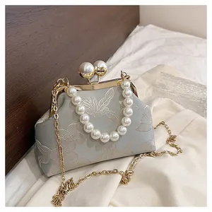 Detalle de bolso bordado azul claro con perlas grandes y cadena de metal dorado