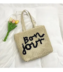 Close-up of handmade straw tote bag featuring black Bon jour embroidery on beige woven texture