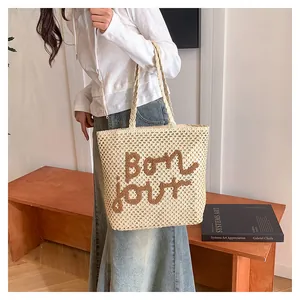 Close-up of beige woven tote bag with Bonjour embroidery and textured straw finish