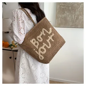 Detail of hollow straw tote bag featuring Bon Jour embroidery and woven shoulder strap