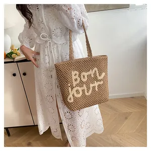 Detail view of woven straw tote bag featuring white 3D Bon jour embroidery and long handles