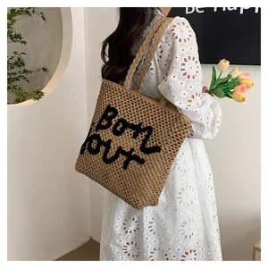 Detail of hollow straw tote bag with black Bonjour embroidery and woven shoulder strap