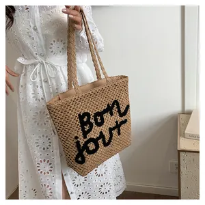 Detail of hollow straw tote bag with black Bonjour embroidery and long shoulder straps