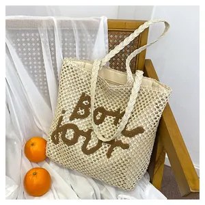 Detail of hollow straw tote bag featuring brown Bonjour embroidery and woven texture