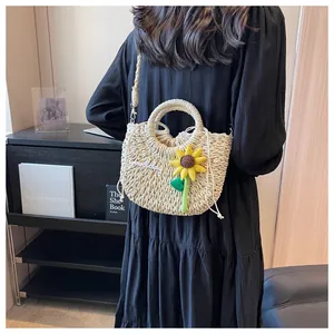 Detailed close-up of woven cream straw bag with sunflower pendant and Goodday embroidery
