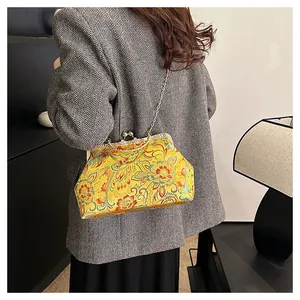 On-shoulder view of a yellow floral silk embroidery bag with a gold chain strap