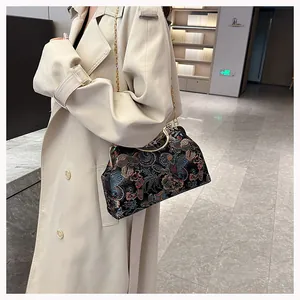 Detail of vintage floral embroidery on a black handbag with metal handle and chain strap