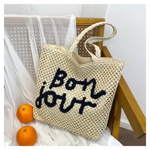 Detail of hollow straw tote bag featuring Bonjour embroidery and fabric lining