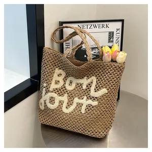 Detailed close-up of straw beach tote with embroidered bon jour text on metal table