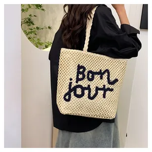 Detail of a beige woven tote bag with Bonjour embroidery shown on model shoulder