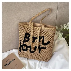 Detailed view of beige hollow straw bag with black embroidered Bonjour lettering