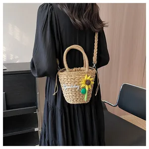 Detail of woven straw bucket bag with sunflower charm and Goodday embroidery worn crossbody