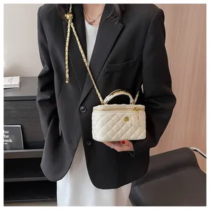 Detail of white quilted mini box bag with gold floral clasp and chain strap on a model