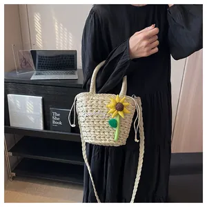 Detail of straw bucket bag with sunflower charm and Goodday embroidery held by model