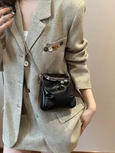 Mini borsa a secchiello nera lucida con catena d'argento su giacca di tweed beige