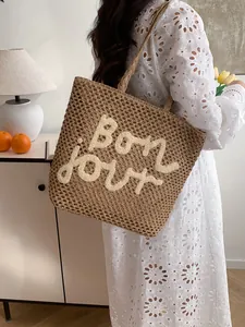 Brown straw tote bag with Bonjour embroidery shown on model in white dress