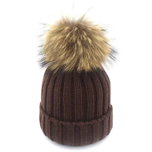 Detailaufnahme der tiefbraunen Strickmütze mit einem großen, flauschigen Pelzbommel