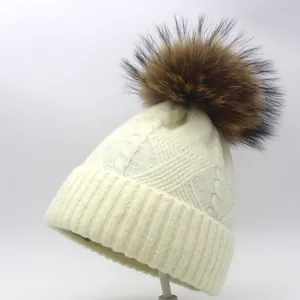Detail of cream cable knit beanie featuring thick ribbed cuff and real fur pompom