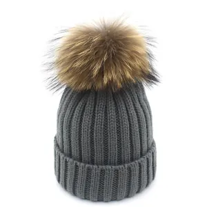 Detail einer grauen Strickmütze mit einem flauschigen braunen Pelzbommel oben