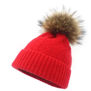 Macro shot of red knit beanie featuring thick cable patterns and soft fur pom-pom