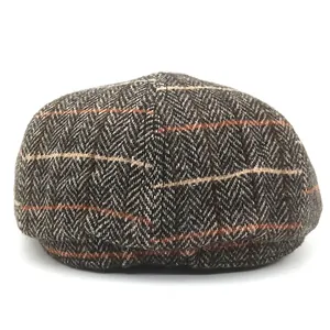 Detail of herringbone tweed newsboy cap showing thick wool texture and orange stripe accents