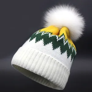 Gestrickte Beanie mit gelb-grünem Zickzackmuster und großem weißen Kunstfell-Bommel