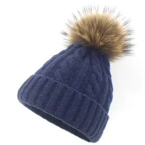 Close-up of cable-knit texture and large raccoon fur pom-pom on navy winter beanie