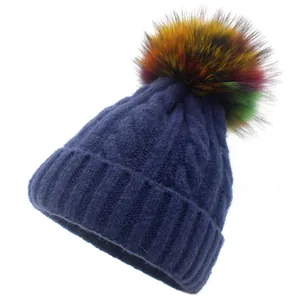 Close-up of navy blue cable-knit beanie featuring a vibrant multi-colored faux fur pom-pom