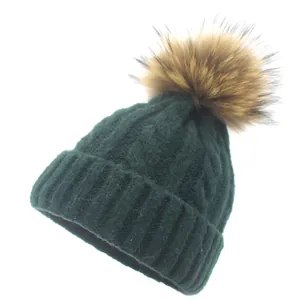 Detailed cable knit pattern on a dark green winter beanie with a fluffy faux fur pom-pom
