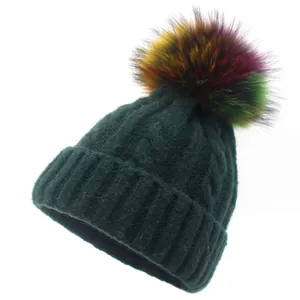 Close-up of dark green cable knit beanie featuring a colorful gradient pom-pom
