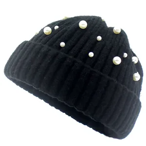 Détail d'un bonnet en maille côtelée noire orné d'élégantes perles blanches sur fond blanc