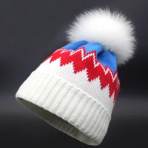 Dreifarbige Strickmütze mit blauem und rotem Zickzackmuster und weißem Kunstfell-Bommel