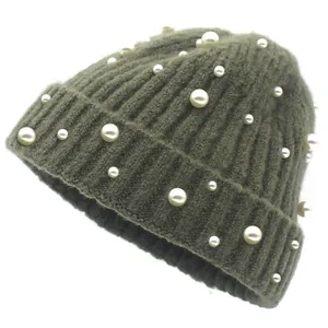 Détail du bonnet en maille vert foncé avec perles blanches et texture tricotée épaisse