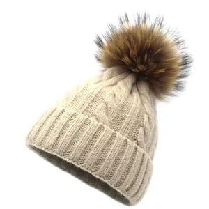 Detail of apricot cable knit beanie with fluffy raccoon fur pompom and wide folded cuff