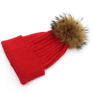 Detail of red ribbed knit beanie with a fluffy dark brown fur pompom on top
