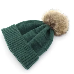 Deep green knit beanie with fluffy faux raccoon pompom and ribbed texture for winter warmth