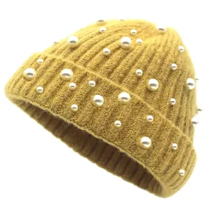 Détail d'un bonnet en maille jaune moutarde orné d'élégantes perles blanches de luxe