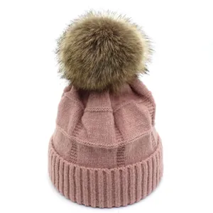 Detail showing dusty pink knit beanie texture and fluffy faux fur pompom ball on top