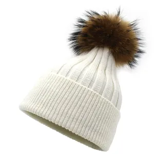 Close-up of ribbed knit winter hat featuring a fluffy raccoon fur pompom in cream white