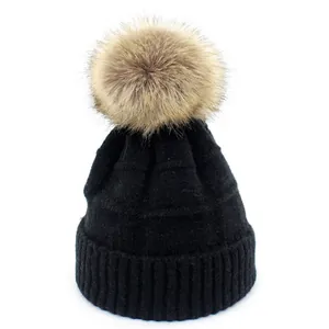 Detail of black knit beanie featuring a large fluffy faux fur pom-pom and ribbed edge