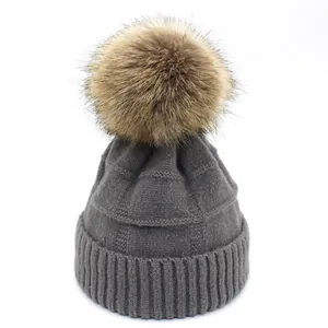 Detail of dark grey knit wool hat with textured check pattern and large brown pom-pom