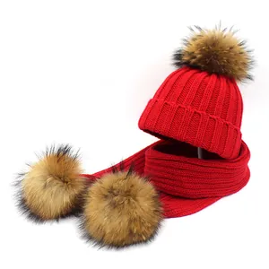 Detail of red cable-knit hat and scarf set featuring three fluffy faux fur pom-poms